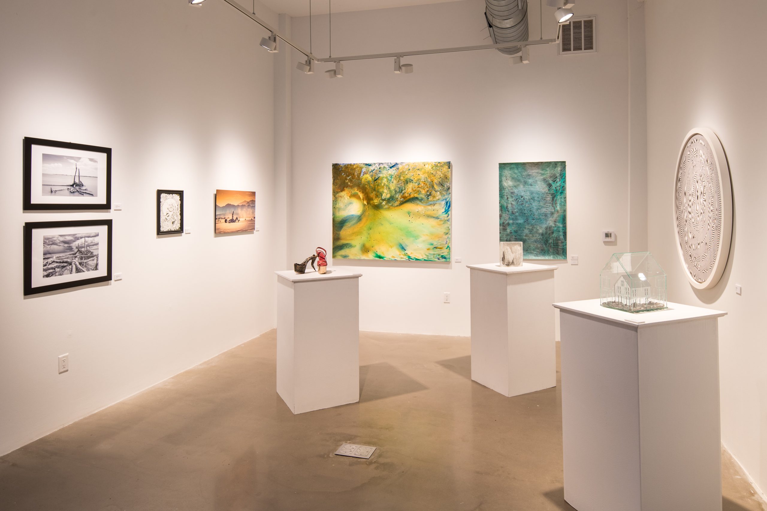 an art gallery with several works displayed on white walls and pedestals.
