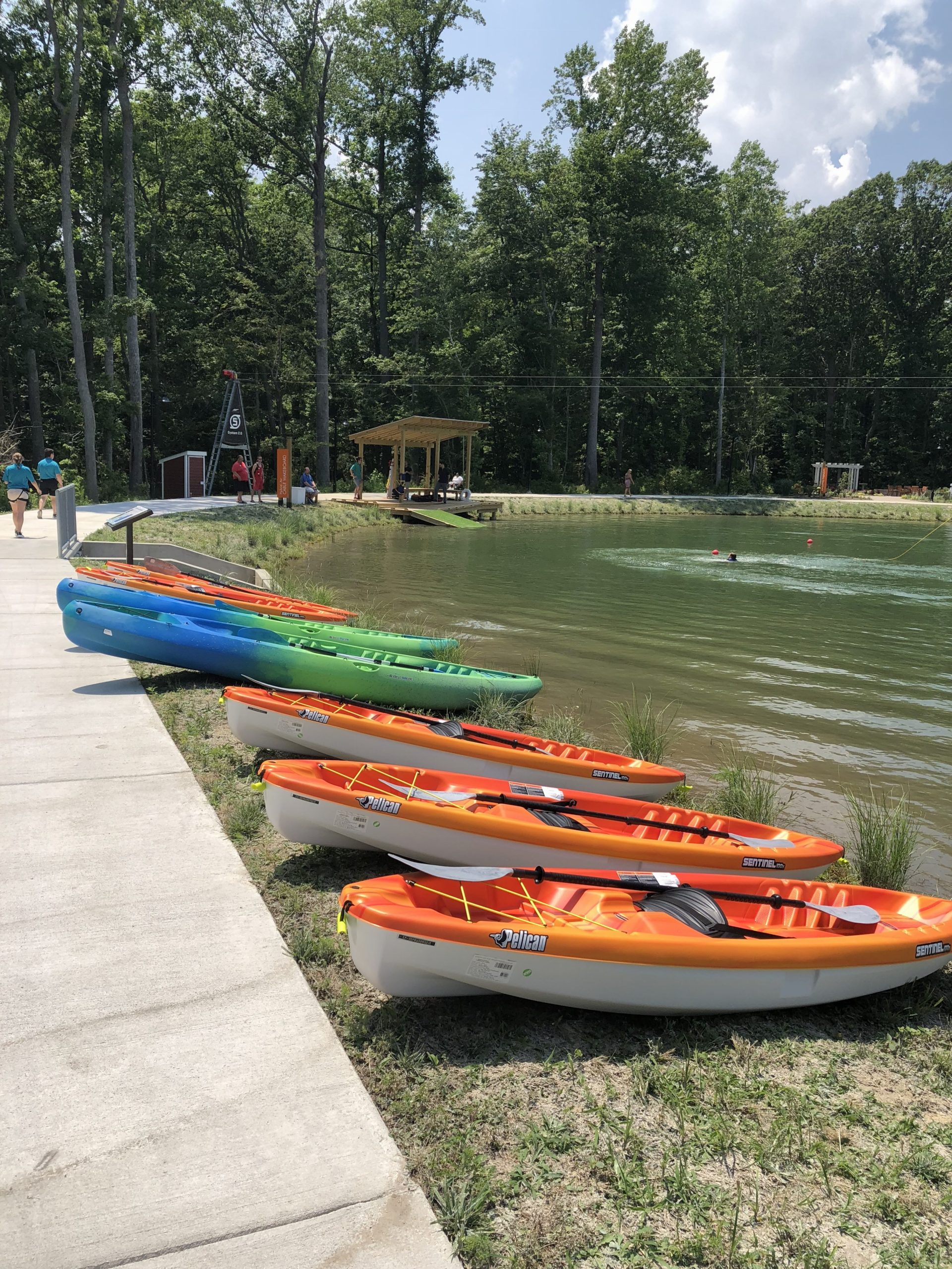 Kayaks lined up along the shore with people on the dock.